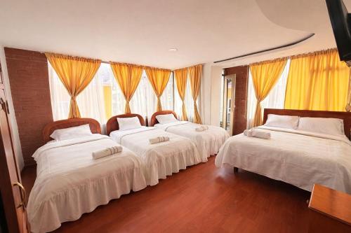a group of four beds in a room with windows at Hotel Dinastia in Ipiales
