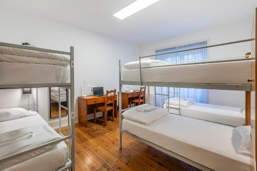 a room with three bunk beds and a desk at HI Coimbra - Pousada de Juventude in Coimbra