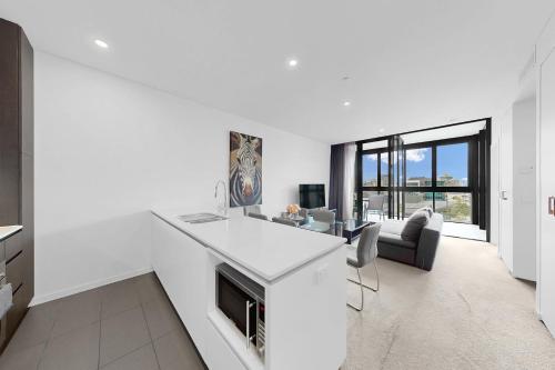 a white kitchen with a desk and a living room at Elegant Urban Hideaway - Private Luxury Residential Apartment, walk to South Bank & Free Carpark in Brisbane