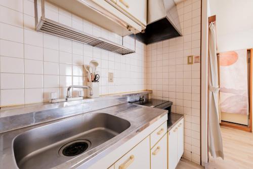 a kitchen with a stainless steel sink and white tiles at Villa Fuchu Stay in Fuchu