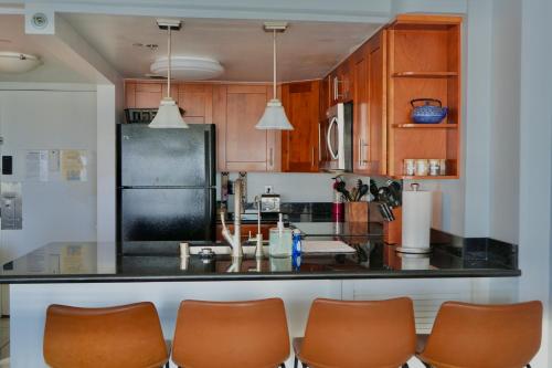 a kitchen with a black counter and some brown chairs at Ilikai Hotel Condo with Kitchen and Ocean View in Honolulu
