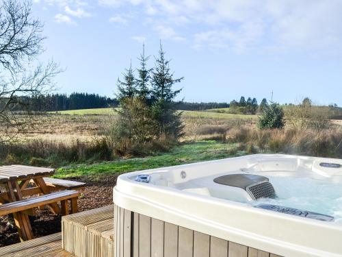 a jacuzzi tub on a deck next to a picnic table at Ochiltree Cottage - Uk7781 in Newton Stewart