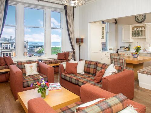 a living room with couches and a table and windows at The Golf Place in St. Andrews