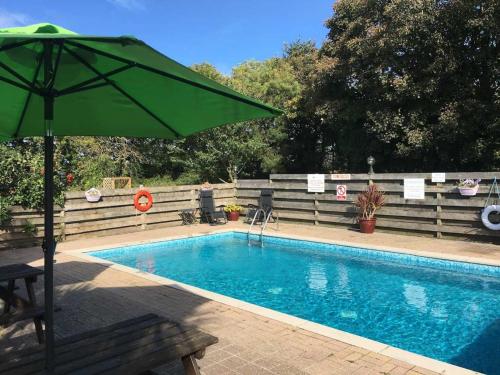 a swimming pool with a green umbrella and a bench at Towan Cottage - Cwc79064 in Perranporth