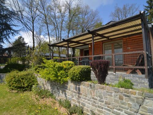 a log cabin with a stone retaining wall and a porch at Comfortable chalet in Petit Han with garden and barbecue in Durbuy
