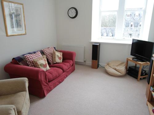 a living room with a red couch and a tv at Monastery 13 - Abbots Rest - Ukc4886 in Fort Augustus