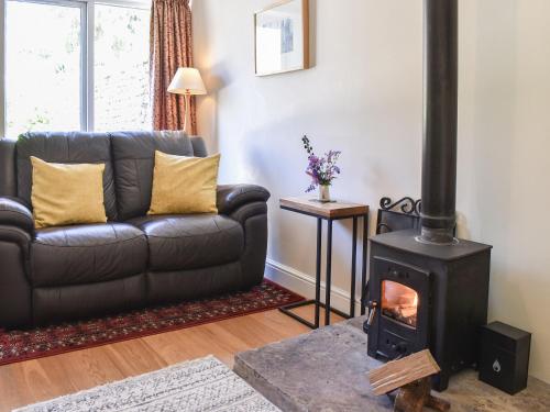 a living room with a leather couch and a wood stove at Acorn Cottage in Ashover