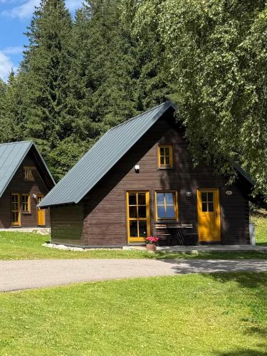 a small wooden house with yellow doors and trees at Chalets & Apartments - Base Camp Medvědín in Špindlerův Mlýn