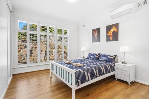 a white bedroom with a bed and some windows at Fairlight Luxe Escape 4BR with Parking in Killara