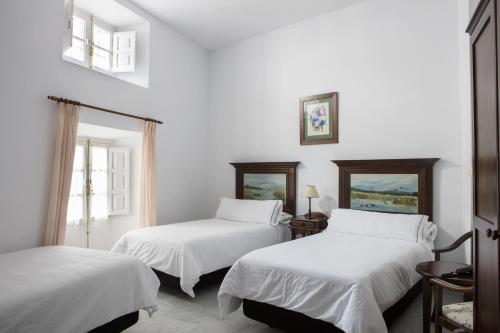 two beds in a room with white walls and windows at Hotel Tugasa Casa Palacio Medina Sidonia in Medina Sidonia