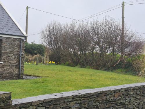 a stone wall in front of a yard with trees at Skellig View in Portmagee