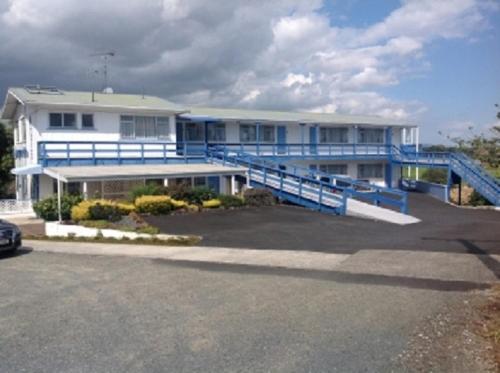 a large white house with a blue railing in a parking lot at Dargaville Motel in Dargaville