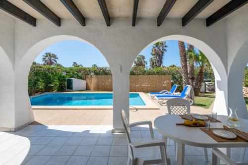 a patio with a table and chairs and a swimming pool at Villa Flor by 3VILLAS in Cala en Bosc