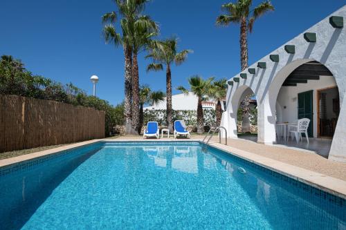 a swimming pool with two chairs and palm trees at Villa Flor by 3VILLAS in Cala en Bosc