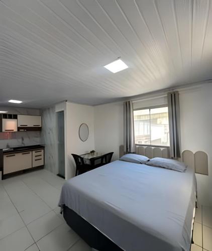 a bedroom with a large white bed and a kitchen at Studio luxo Periperi in Salvador