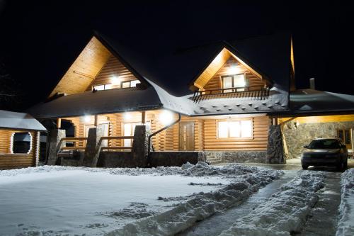 a wooden house with snow on the roof at night at Sadyba Pikuy in Bilasovytsya