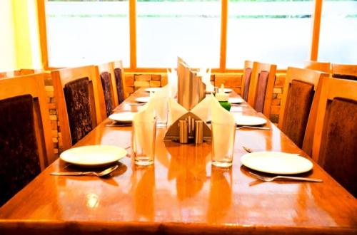 a long wooden table with plates and napkins on it at Hotel tridev in Manāli
