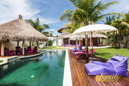 a pool at a resort with purple chairs and umbrellas at Villa Kaaiti in Uluwatu