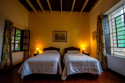two beds in a room with two windows and two lamps at Casa Hacienda Majoro in Nazca