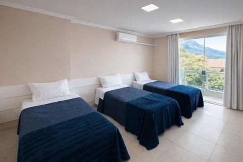 two beds in a room with a large window at Apê 301 - Central, Garagem, Ar-Cond - 2 Quartos in Governador Valadares