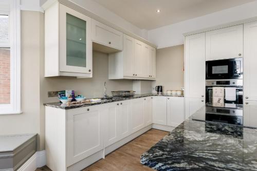 a white kitchen with white cabinets and black appliances at Park Lake View - Poole Park Lake Views in Poole