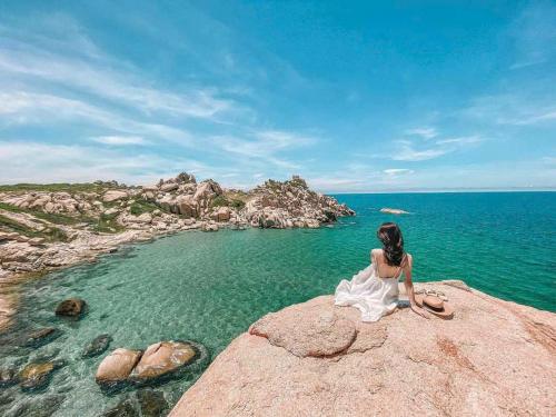 a woman sitting on a rock overlooking the ocean at Phong Dung Beach Hotel Phan Ri Cua in Tuy Phong
