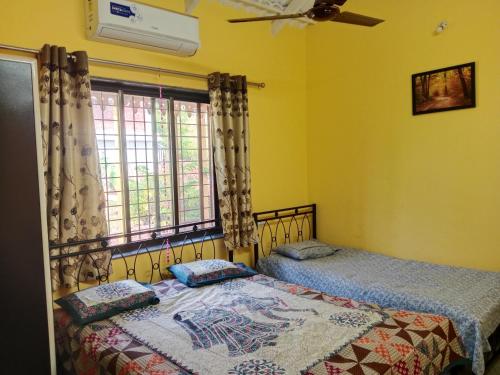 two beds in a room with yellow walls and a window at Fulora Guesthouse in Dapoli