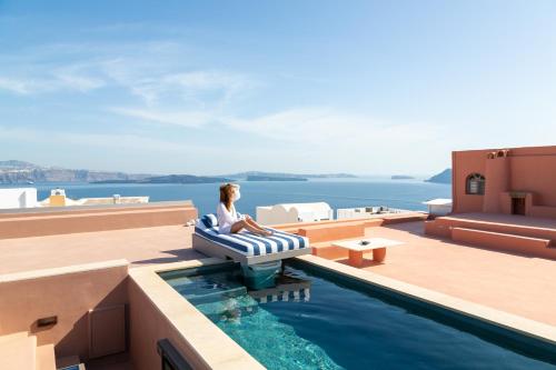 a woman sitting on a chair next to a pool on a building at Villa Oro in Oia