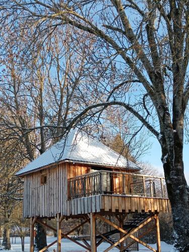 a tree house with a deck in the snow at Chalets et cabane perchée "Ô Cœur des Puys" in Ceyssat