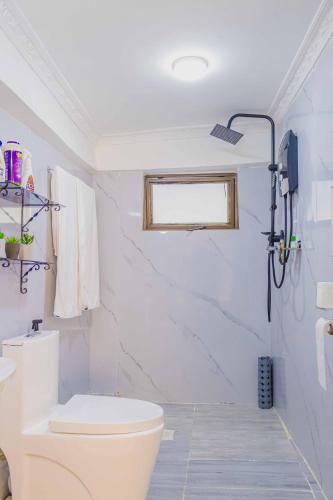 a white bathroom with a toilet and a window at Chic Modern Studio Apartment with Pool in Nanyuki