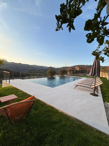 a swimming pool with two lawn chairs and an umbrella at Estrela do Gerês - Casa Fernandes in Outeiro
