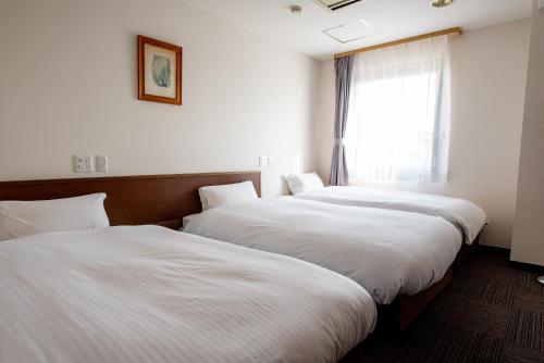 two beds in a hotel room with a window at 小牧シティホテル in Komaki