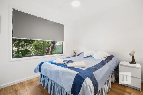 a white bedroom with a bed with a window at Garden Cottage Noraville in Toukley