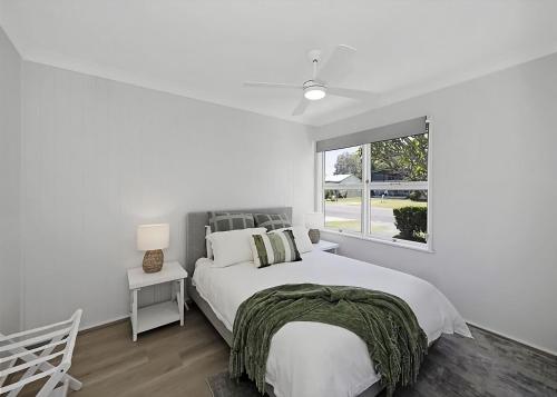 a white bedroom with a large bed and a window at Frangipani Hideaway in Budgewoi