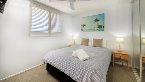 a white bedroom with a bed and a window at Merrima Court Holidays in Caloundra
