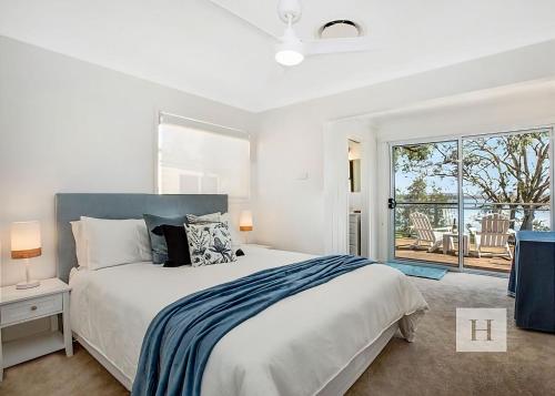 a white bedroom with a bed and a large window at Niaroo Lakeside in Summerland Point