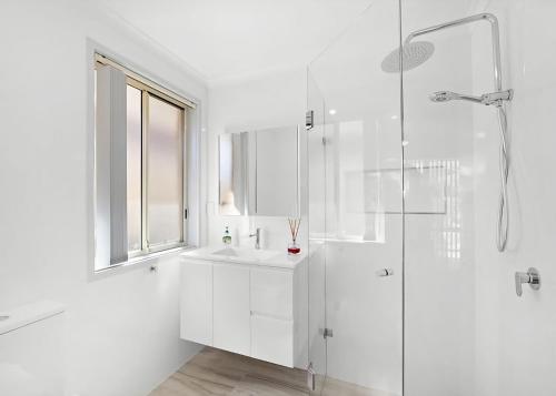 a white bathroom with a shower and a sink at The Sailor s Haven in Mannering Park