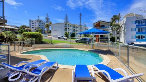 a swimming pool with chairs and an umbrella at Merrima Court Holidays in Caloundra