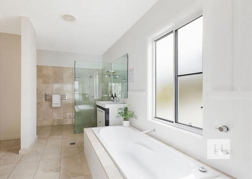 a white bathroom with a large tub and a window at Sunset Central Coast in Mannering Park