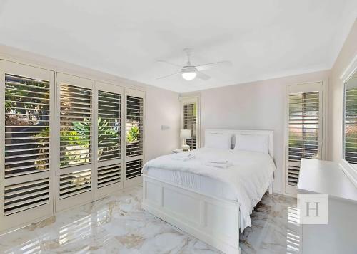 a white bedroom with a white bed and windows at Sunset Lakehouse in Toukley
