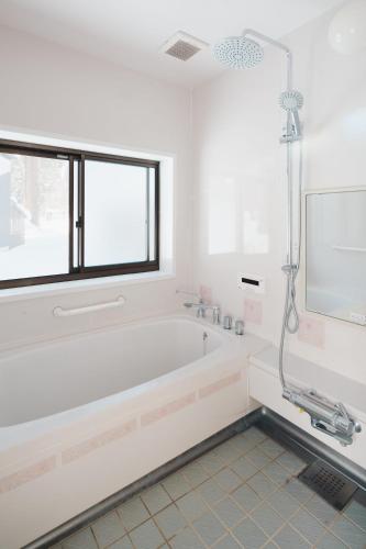 a white bathroom with a tub and a window at Ao No Mori in Myoko
