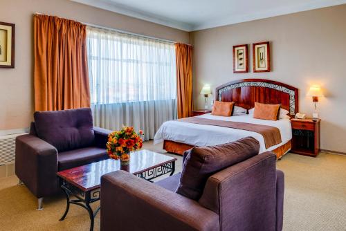 Habitación de hotel con cama, 2 sillas y mesa en Bulawayo Rainbow Hotel, en Bulawayo