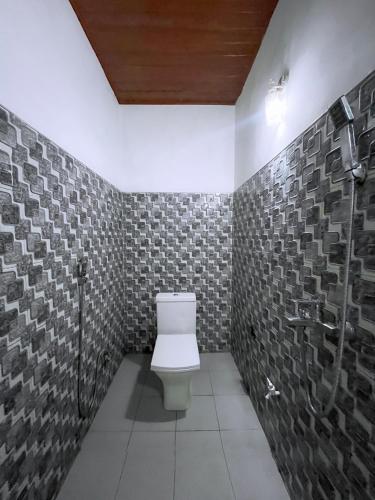 a bathroom with a toilet and a tile wall at The Grand Residence in Ella