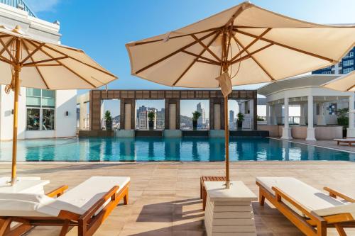 a pool with chairs and umbrellas in front of a building at Cape Racha Hotel in Si Racha