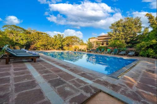 a large swimming pool with chairs and a blue sky at The Pugmark, A Wildlife Resort in Sawāi Mādhopur