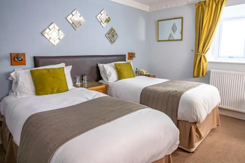 two beds in a hotel room with yellow curtains at New Holmwood Hotel in Cowes
