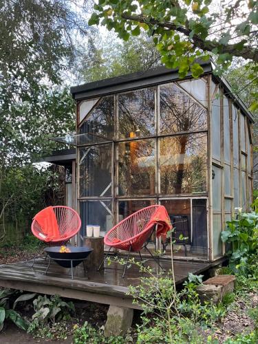 a glass house with two red chairs on a deck at Green Box - be in nature with direct train to Porto in Valongo
