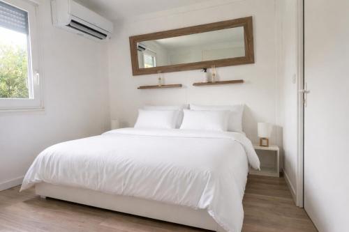 a white bedroom with a white bed and a mirror at Bungalow jacuzzi & jardin privatif séjour détente au soleil in La Crau