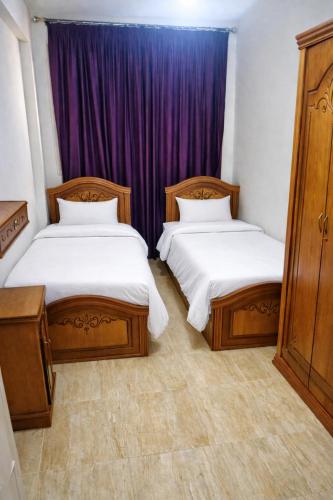 two beds in a room with purple curtains at Lazorde Bay Apartment in El Alamein