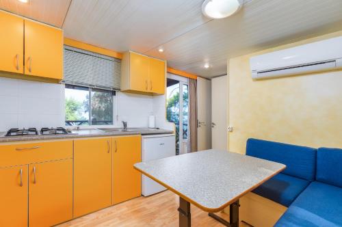 a kitchen with yellow cabinets and a table and a blue couch at Arena Tasalera Mobile Homes in Premantura